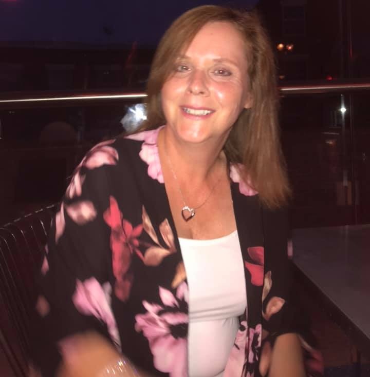 a woman wearing a floral shirt and a heart necklace smiles for the camera