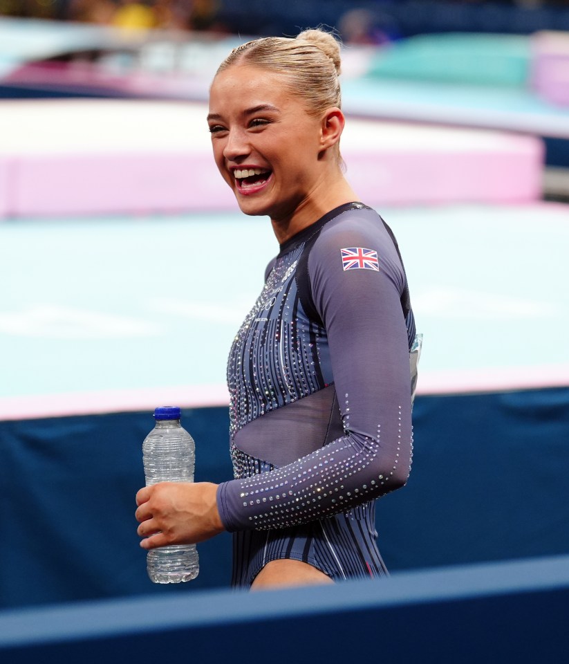 a female gymnast is smiling and holding a bottle of water