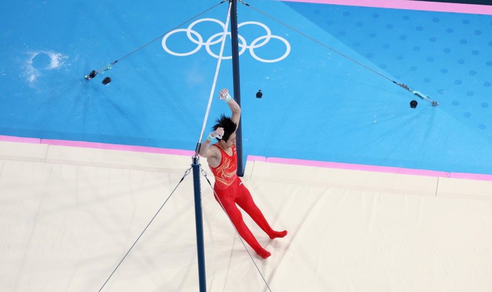 a gymnast performs a trick on a pole with the olympic rings in the background