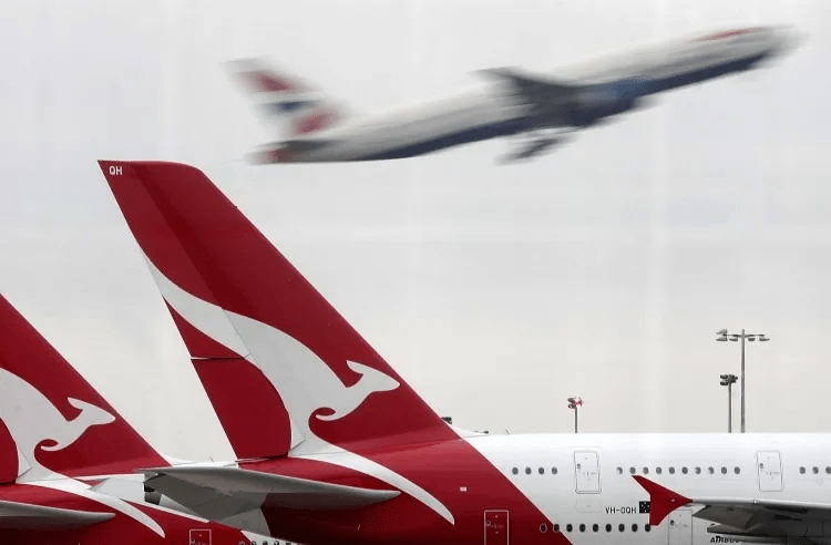 a british airways plane is flying over a row of qantas planes