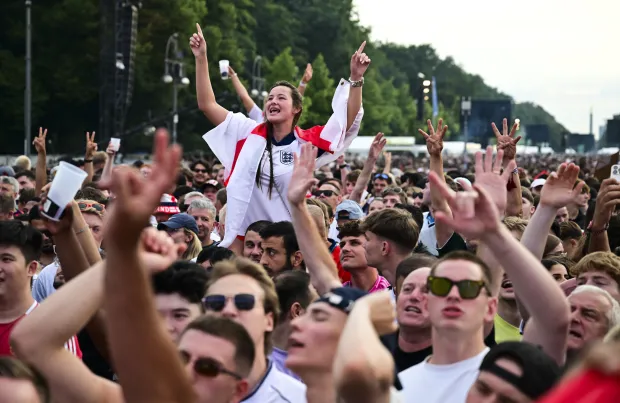 a crowd of people with their hands in the air including a woman wearing a england shirt