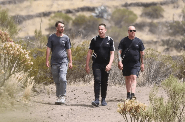 three men are walking down a dirt path and one of them is wearing an adidas shirt