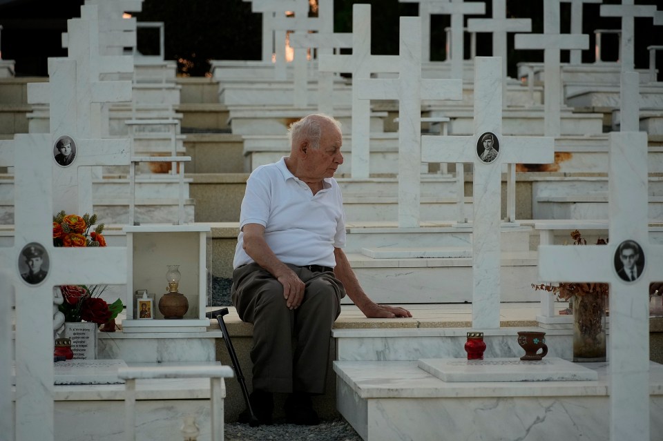 a man sits in a cemetery surrounded by white crosses