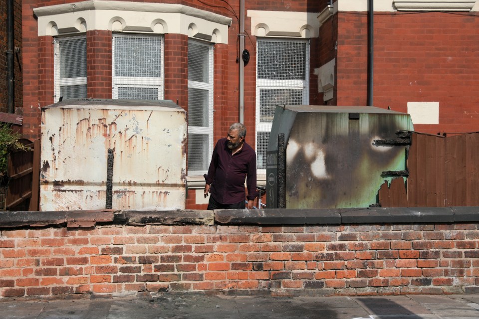 A man inspects damaged clothing bins and a fence of the Southport Islamic Society Mosque