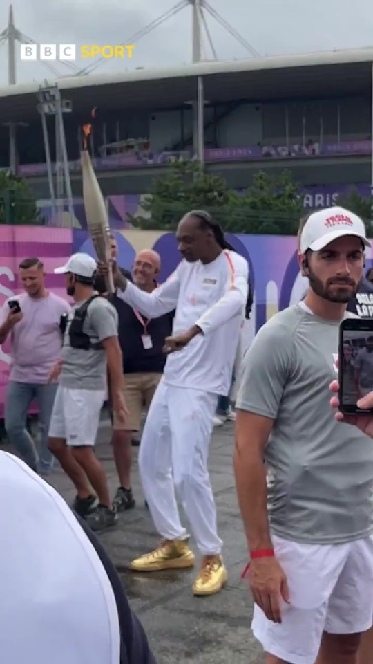 a man in a bbc sport hat holds a torch