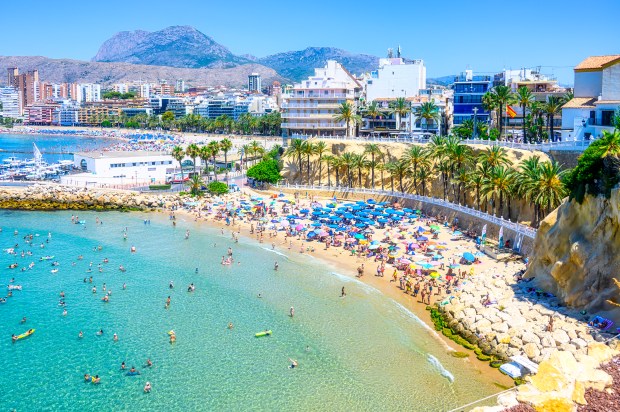 a beach filled with people and umbrellas with mountains in the background