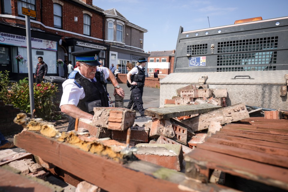 A police community support officer removes bricks from a damaged wall