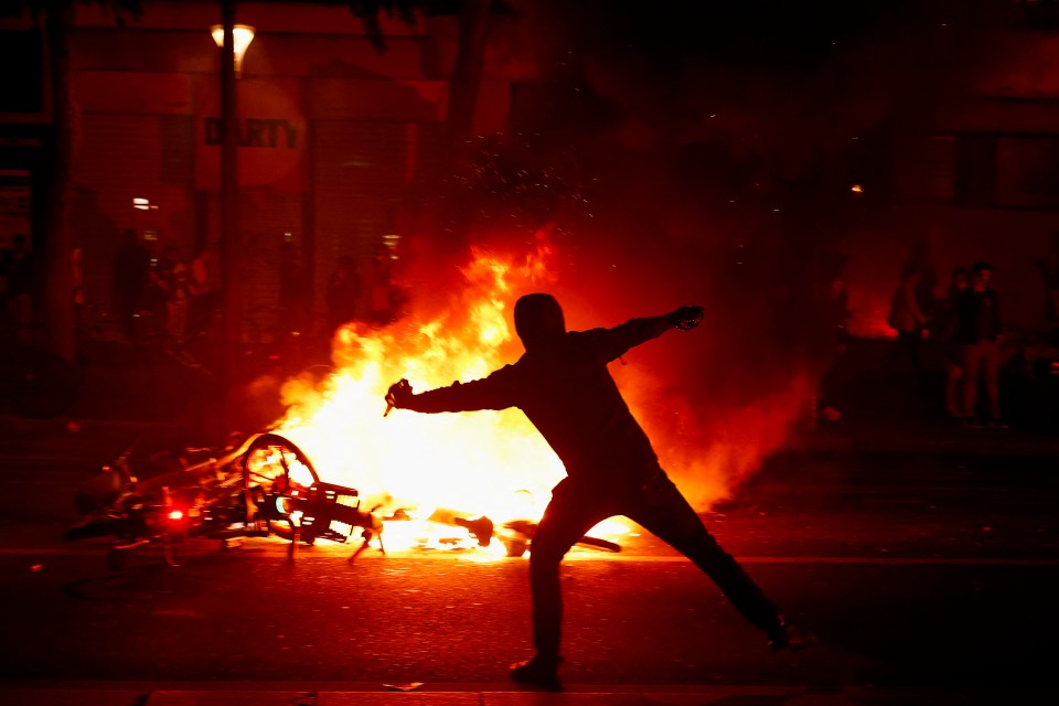 A protester throws a projectile near burning bicycles during clashes with police following partial election results