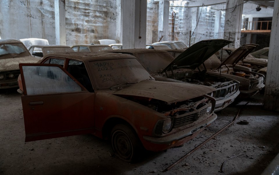 a row of old cars are lined up in a warehouse and one of them has the year 1993 on the windshield