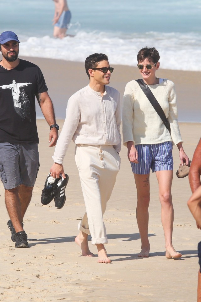 Rami Malek and Emma Corrin stroll along the beach with security close behind