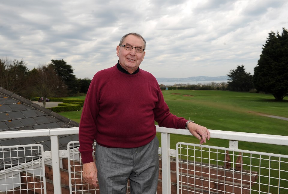 a man in a red sweater stands on a balcony overlooking a golf course