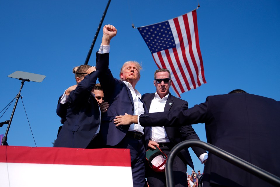 a man in a suit holds up his fist in front of an american flag