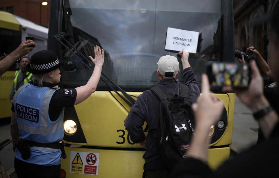 Protesters in Manchester blocked public transport with one man holding up a sign to a tram which read: 'Dismantle GMP now'