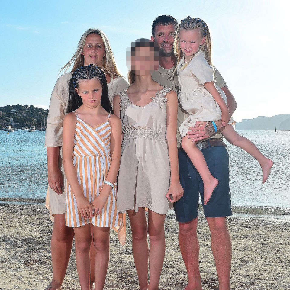 a family poses for a picture on the beach with a man holding a little girl