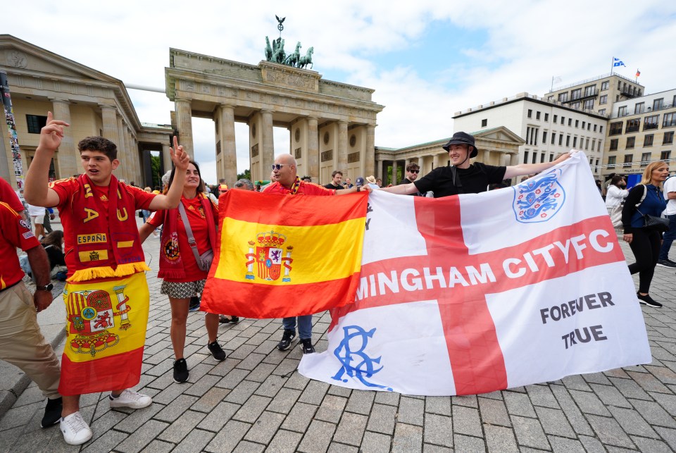 Spain and England fans hold up their national flags as they gather next to the Brandenburg Gate in Berlin, Germany, ahead of the UEFA Euro 2024 final