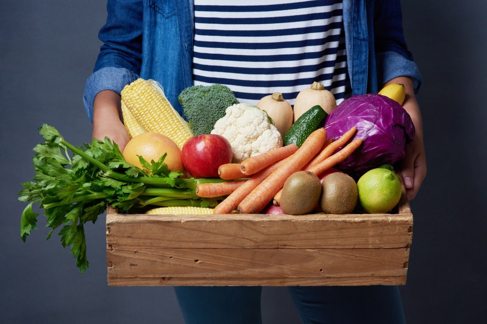 a woman is holding a wooden box full of fruits and vegetables