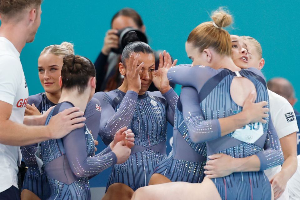 a group of gymnasts are hugging each other and one has a british flag on her shirt