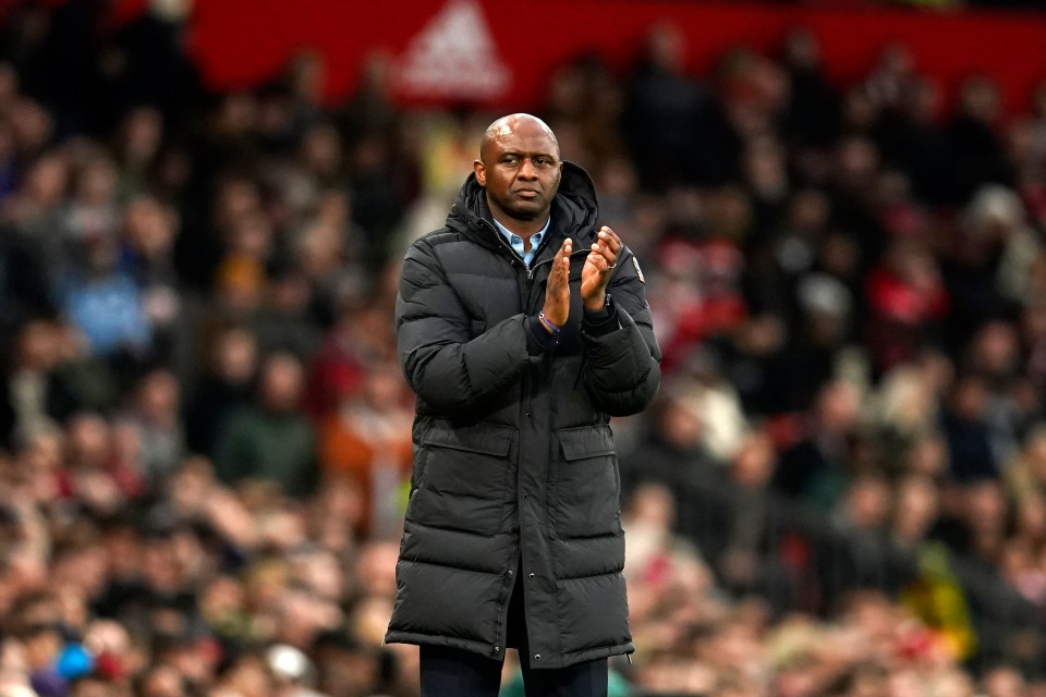 a man in a black jacket applauds in front of an adidas logo