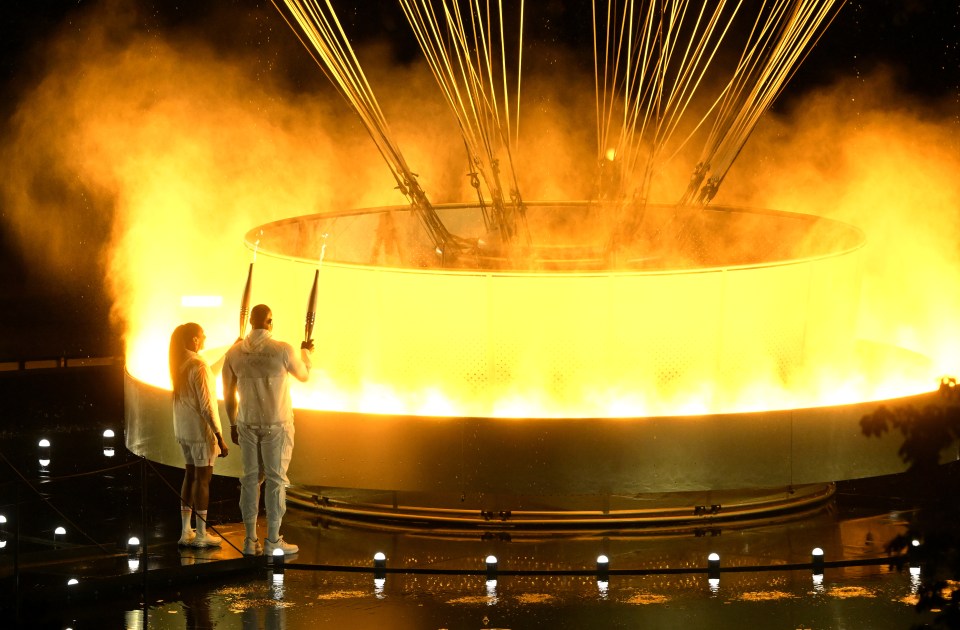 a man and a woman standing in front of a large fire