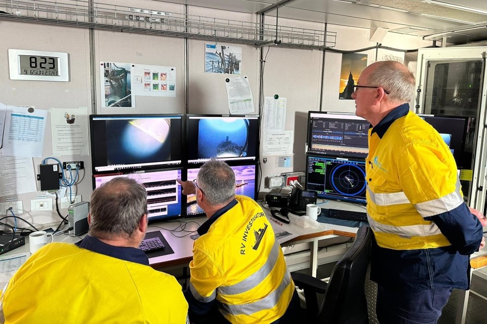 three men in yellow safety vests are looking at computer monitors and one of them is wearing a shirt that says offshore