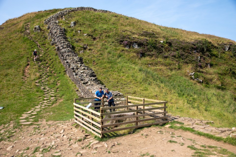 two men standing in front of a stone wall on top of a hill