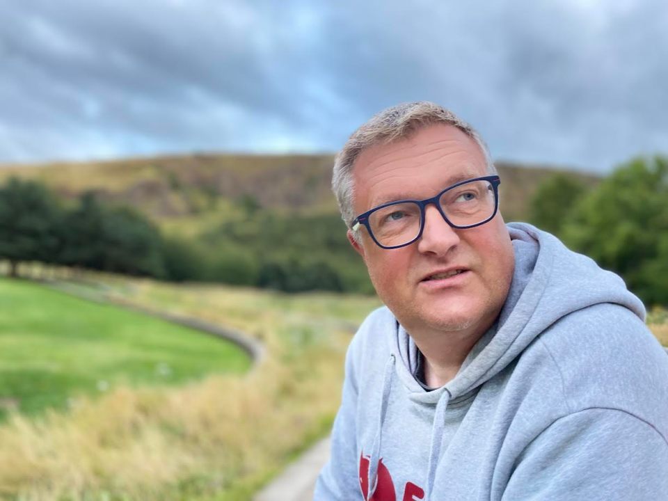 a man wearing glasses and a grey hoodie with the letter a on it