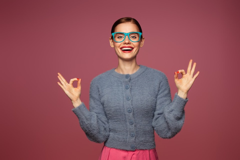 a woman wearing glasses and a blue sweater is giving the ok sign