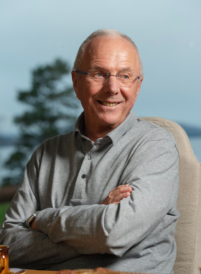 a man in a grey shirt and glasses is smiling with his arms crossed