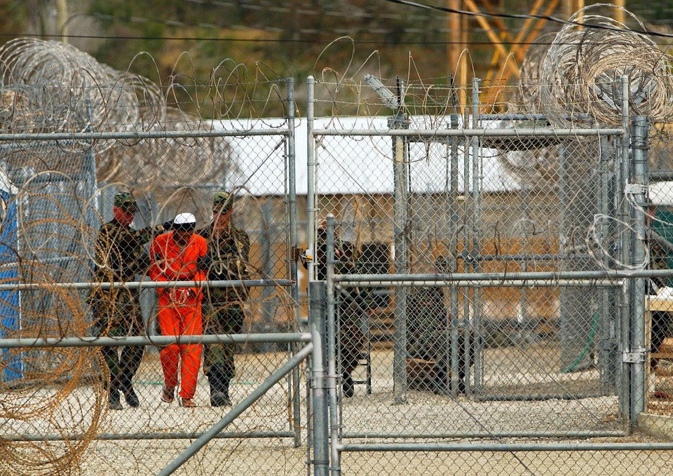 An inmate in an orange jumpsuit is escorted by guards in 2002