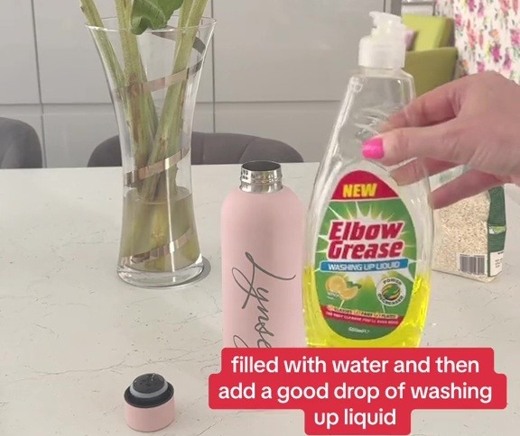 a bottle of elbow grease sits on a counter next to a vase of sunflowers