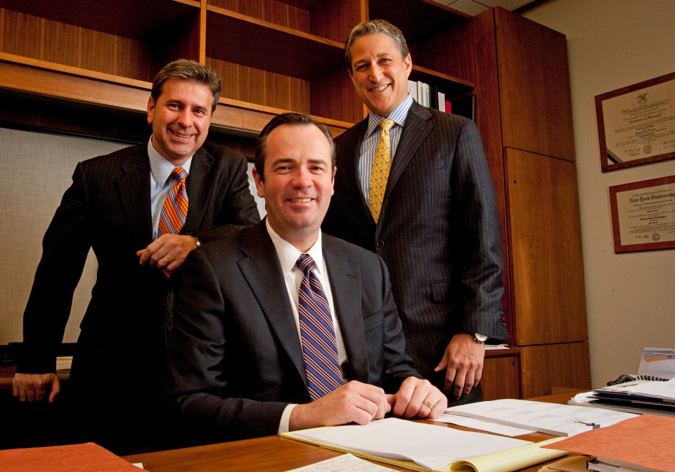 three men in suits and ties pose for a photo in front of a wall with new york university degrees on it