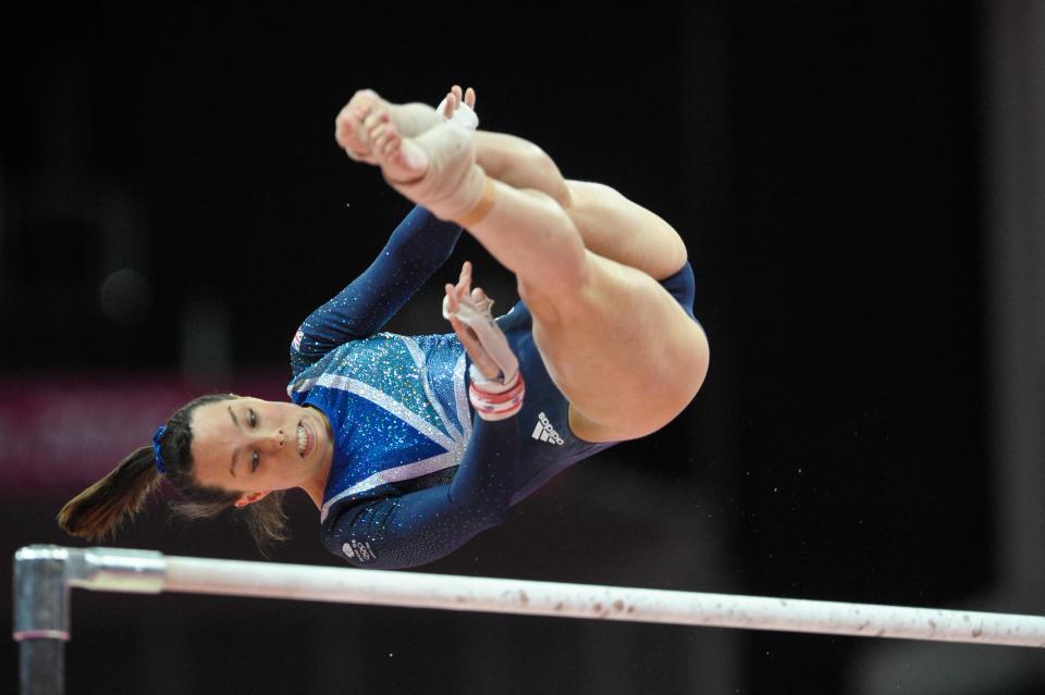 a female gymnast wearing a blue adidas leotard performs on the bars