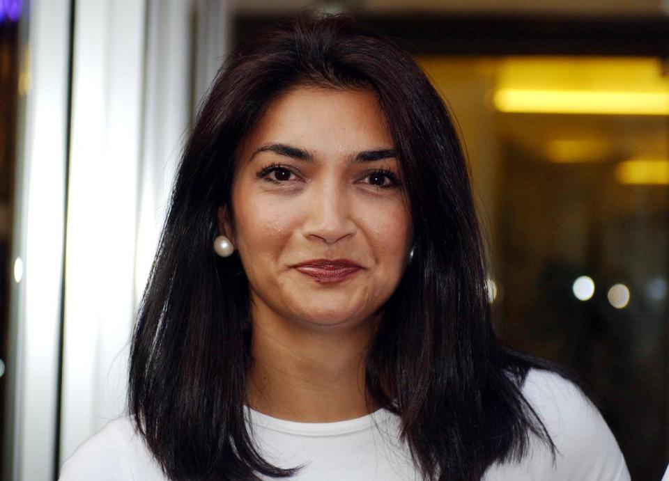 a woman with dark hair and pearl earrings looks at the camera