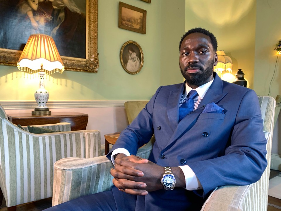 a man in a suit sits in a chair with his hands folded