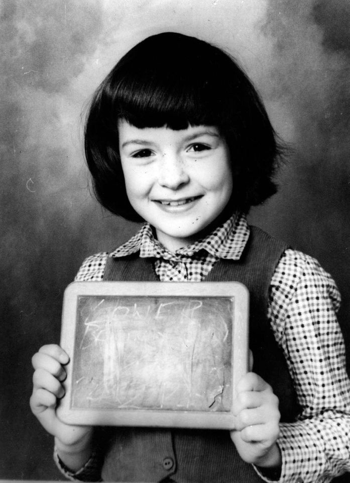 a young girl holds up a chalkboard with the word one written on it