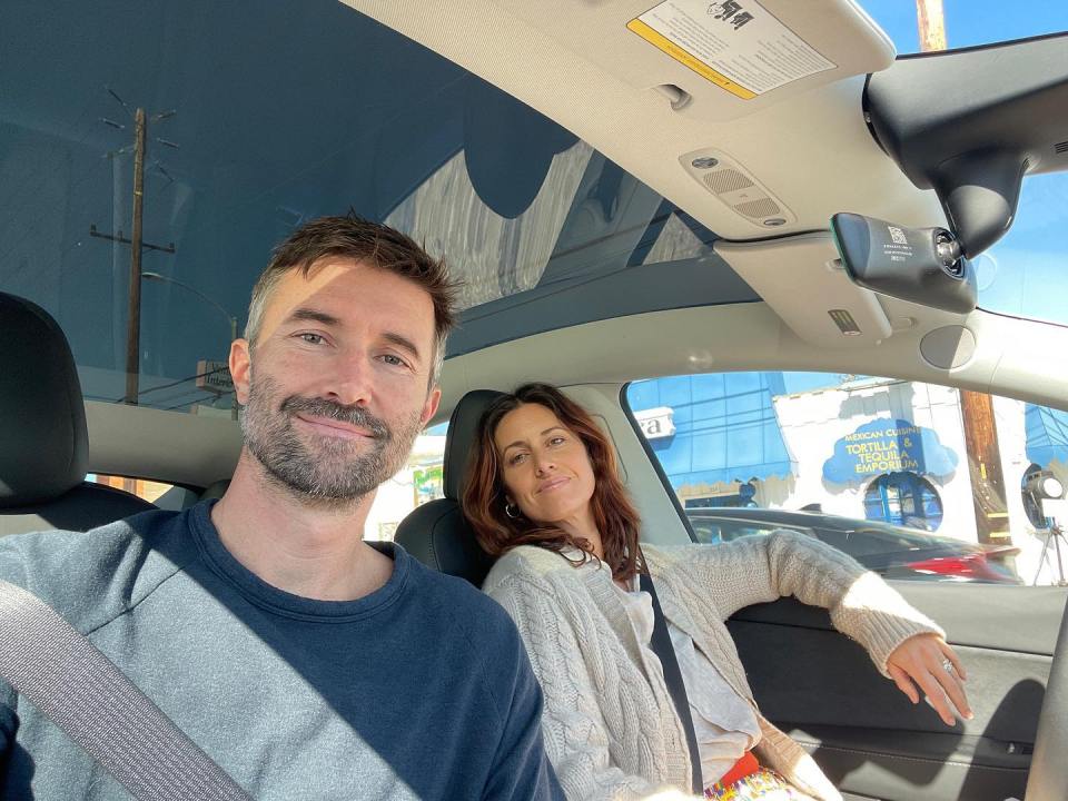 a man and a woman sit in a car with a warning label on the rear view mirror