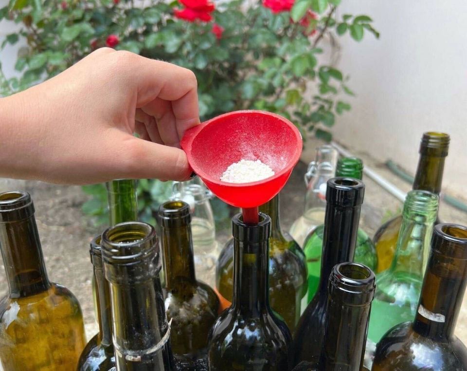 a person pouring something into a wine bottle with a red funnel