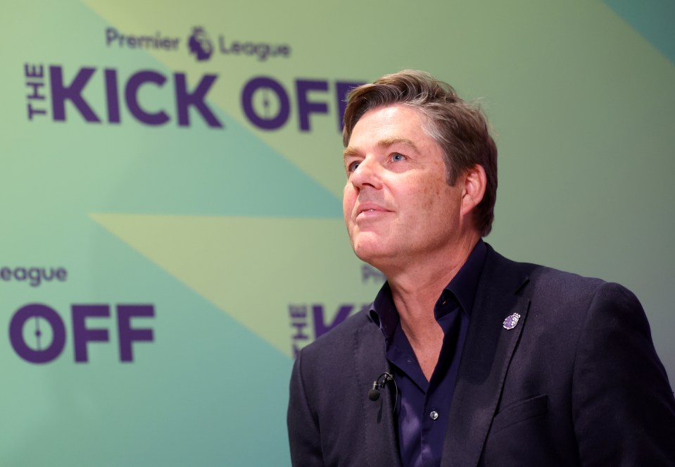 a man stands in front of a premier league kick off sign