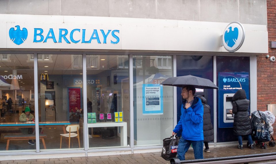 a man holding an umbrella walks past a barclays bank