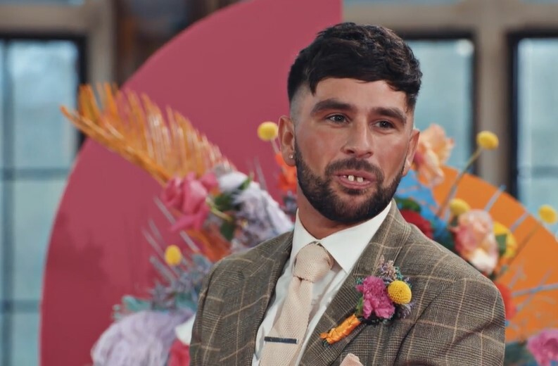 a man in a suit and tie stands in front of flowers