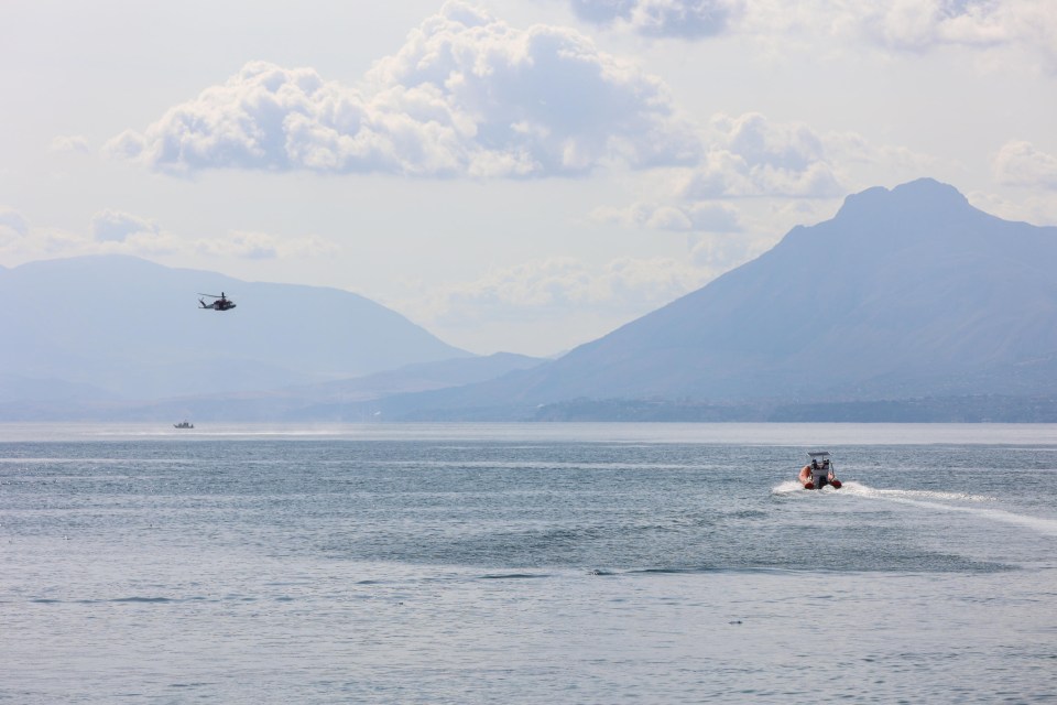 a helicopter flies over a body of water with mountains in the background