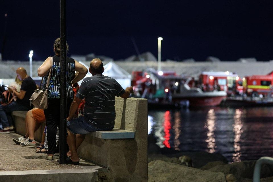 People watch as rescue workers and divers from the Italian fire brigade work