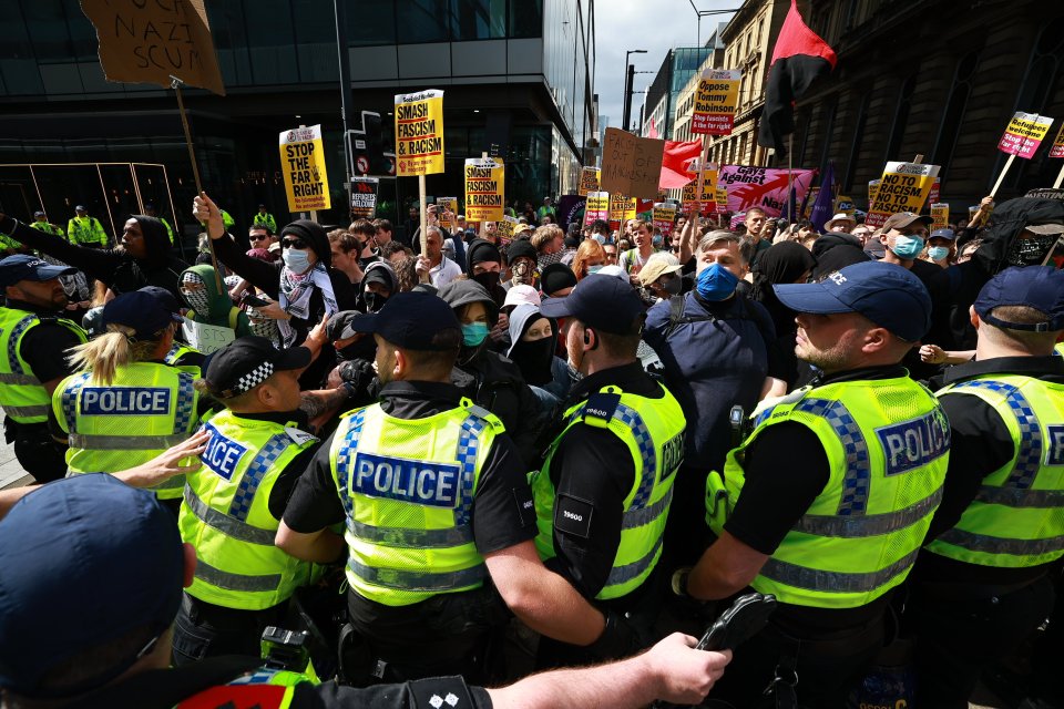 Police officers stand guard as people participate in a protest in Manchester