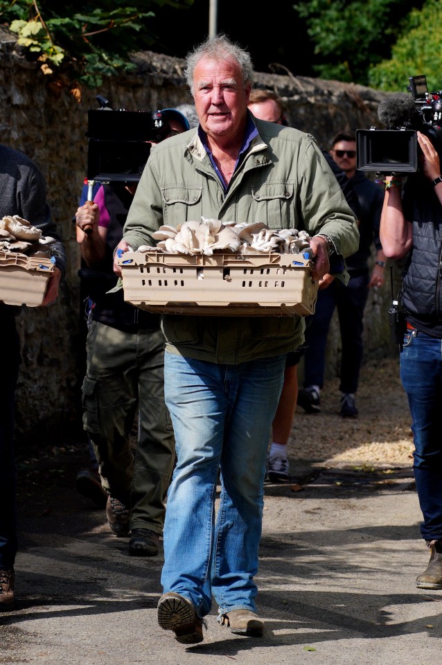 a man in a green jacket is carrying a crate of mushrooms