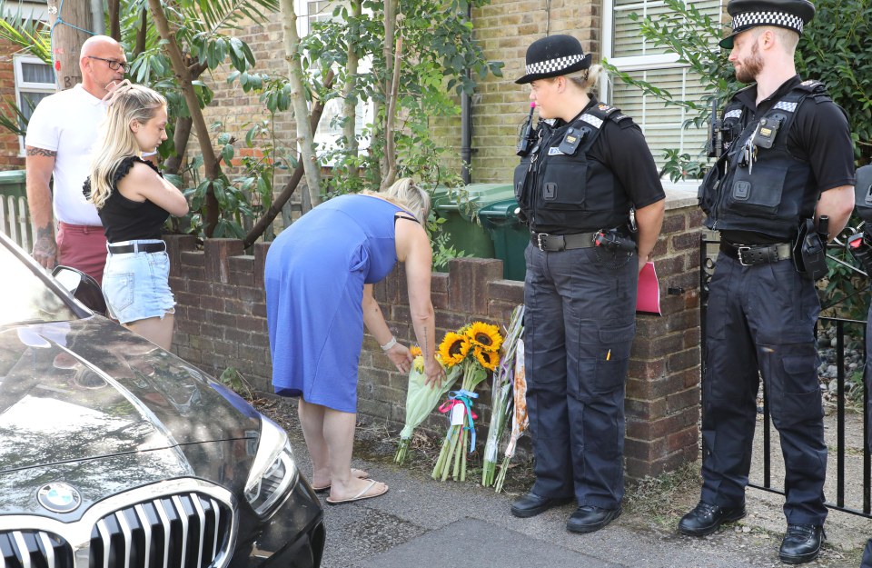 People laying flowers outside the house as officers look on