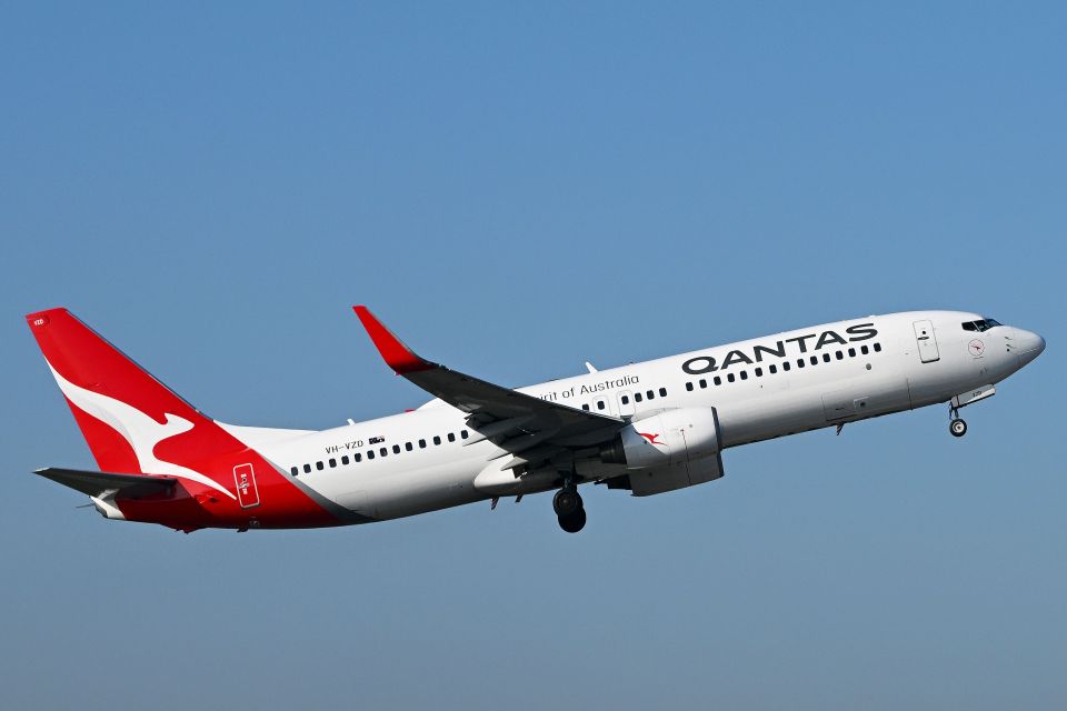 a red and white qantas plane is flying in the sky