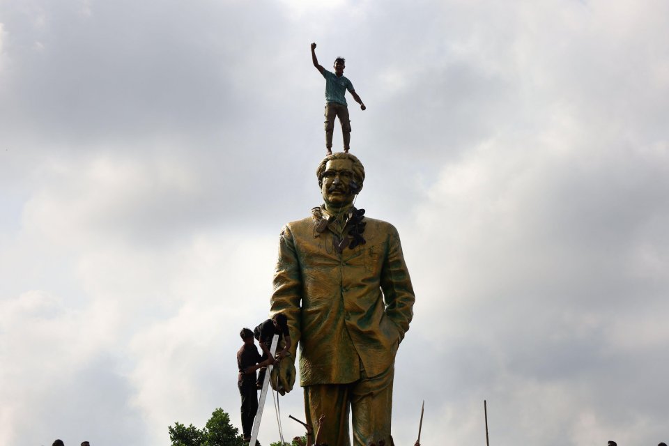 A protester stands on a statue of the prime minister's father, and former leader of Bangladesh