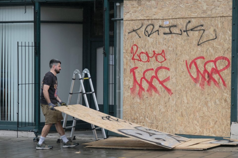 a man is carrying a piece of plywood in front of a building with graffiti on it