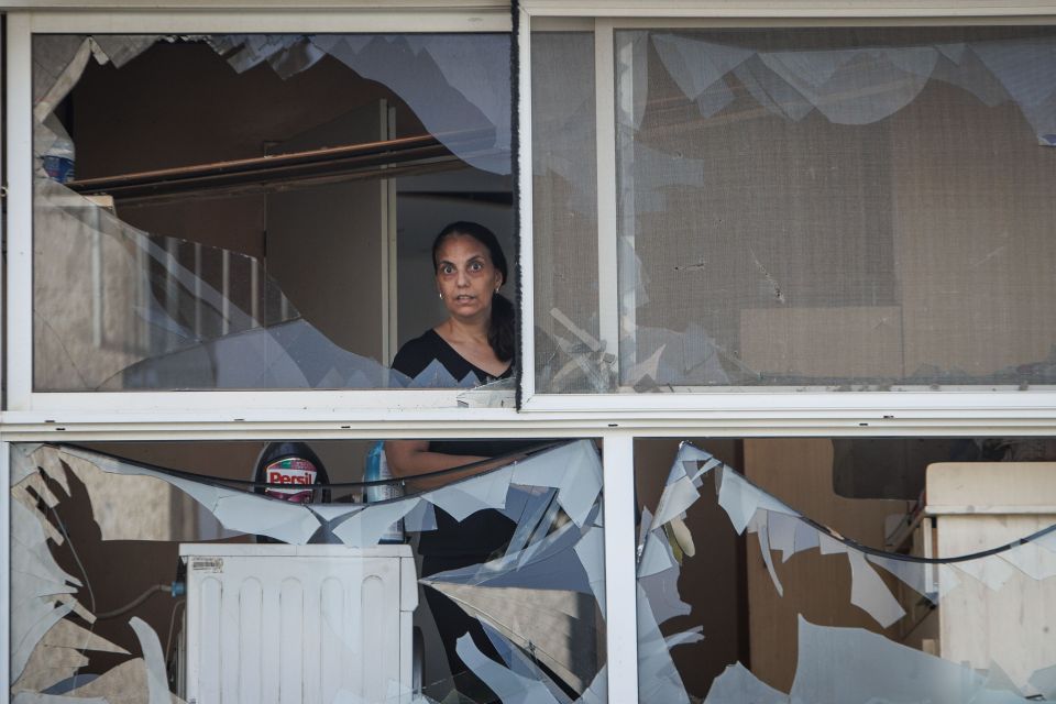 An Israeli woman standing standing near a shattered window in a building hit directly by a Hezbollah rocket