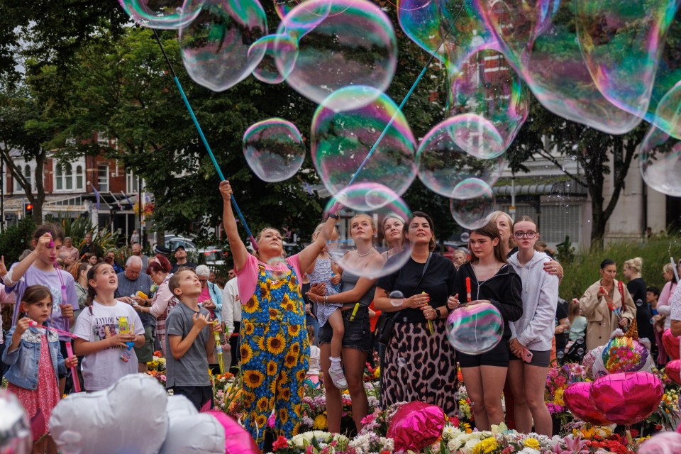 a woman in a sunflower dress blows soap bubbles in front of a crowd